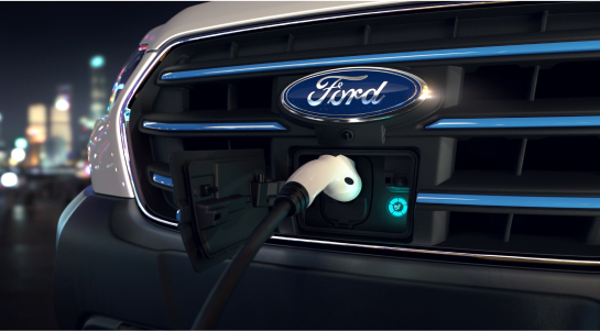 Close-up view of an electric vehicle charging port with a charging cable connected, prominently displaying the Ford logo on the grille.