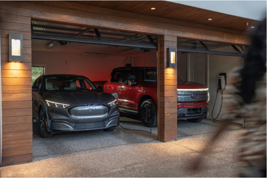 Two electric vehicles, a gray car and a red truck, parked side by side in a modern garage, both connected to charging stations.