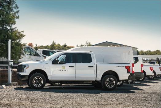 White pickup truck with a canopy parked in a lot alongside other vehicles, under a clear sky.