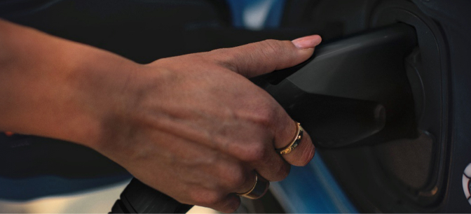 Close-up of a person's hand plugging in a charging cable to an electric vehicle.