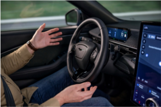 Interior view of an electric vehicle showing hands gesturing freely with no one holding the steering wheel, demonstrating the car’s autonomous driving feature.