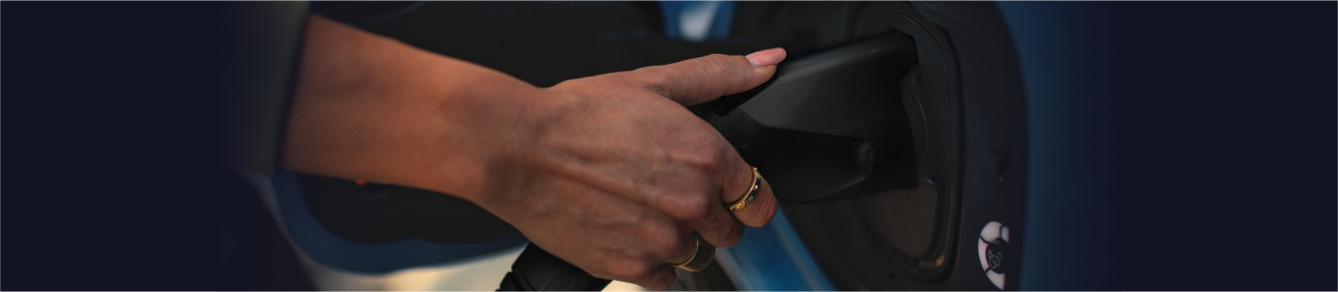 Close-up of a person's hand plugging in a charging cable to an electric vehicle.