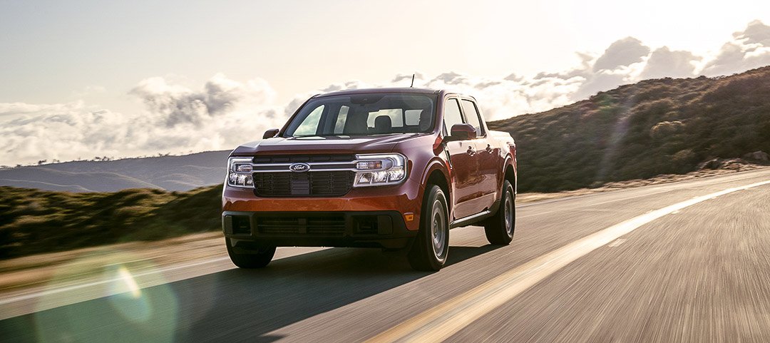 Vue 3/4 avant du Ford Maverick Lariat 2022 rouge roulant sur une route au bord des collines