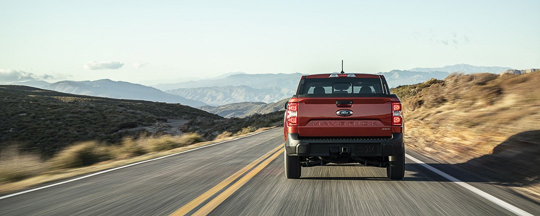 Vue arrière du Ford Maverick Lariat 2022 rouge roulant sur une route dans un désert avec les montagnes au loin