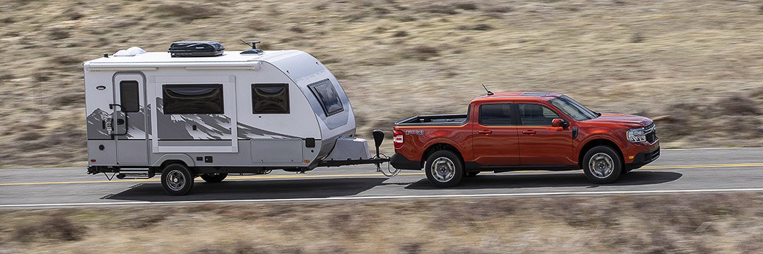 Vue latérale du Ford Maverick Lariat 2022 rouge remorquant une roulotte sur une route dans un désert