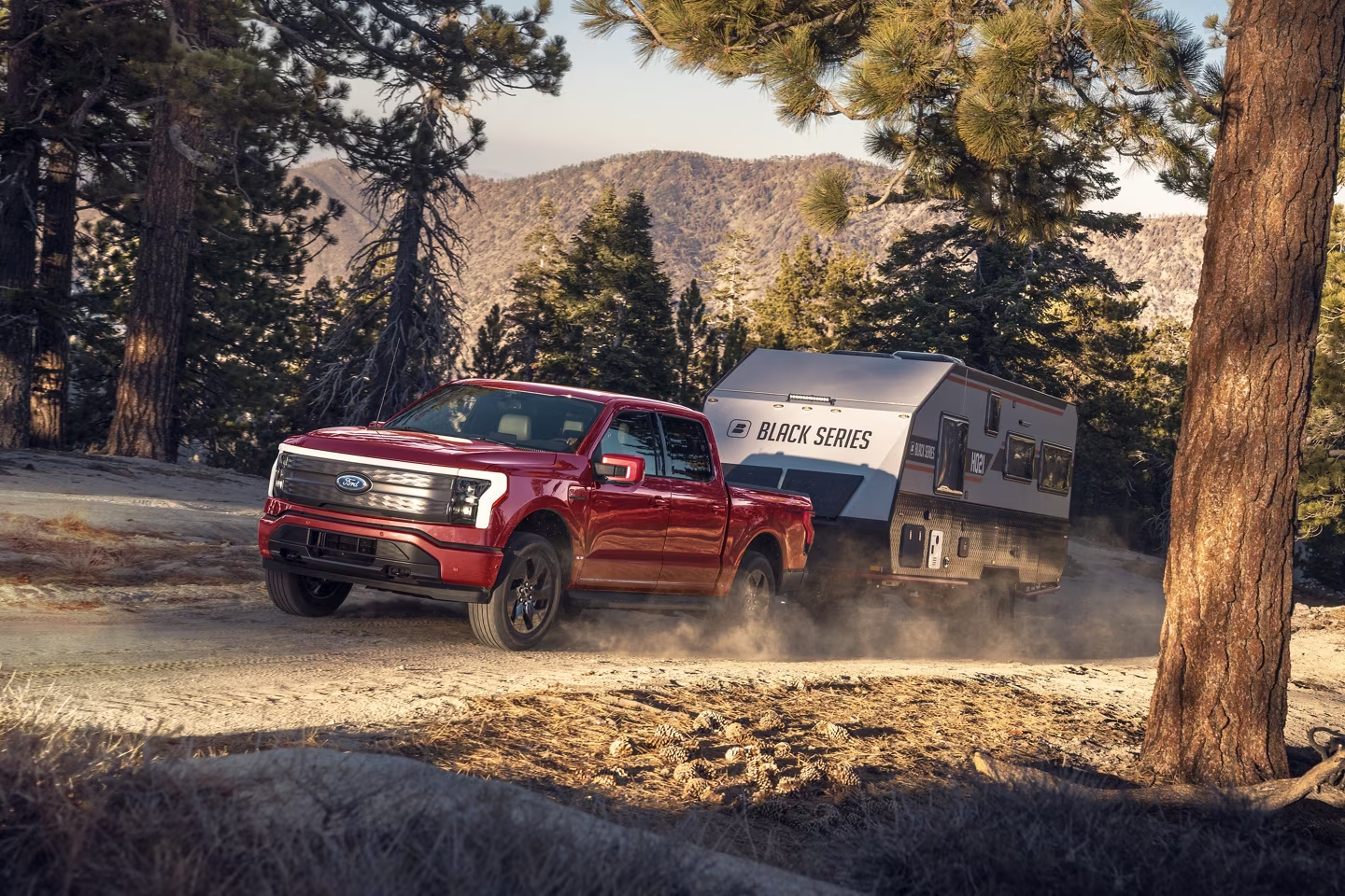 2023 Ford F-150 Lightning towing a camper through the trails of a wooded forest.