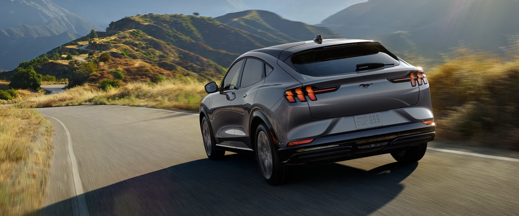 Grey 2023 Mustang Mach-E driving down a curvy road through the mountains.