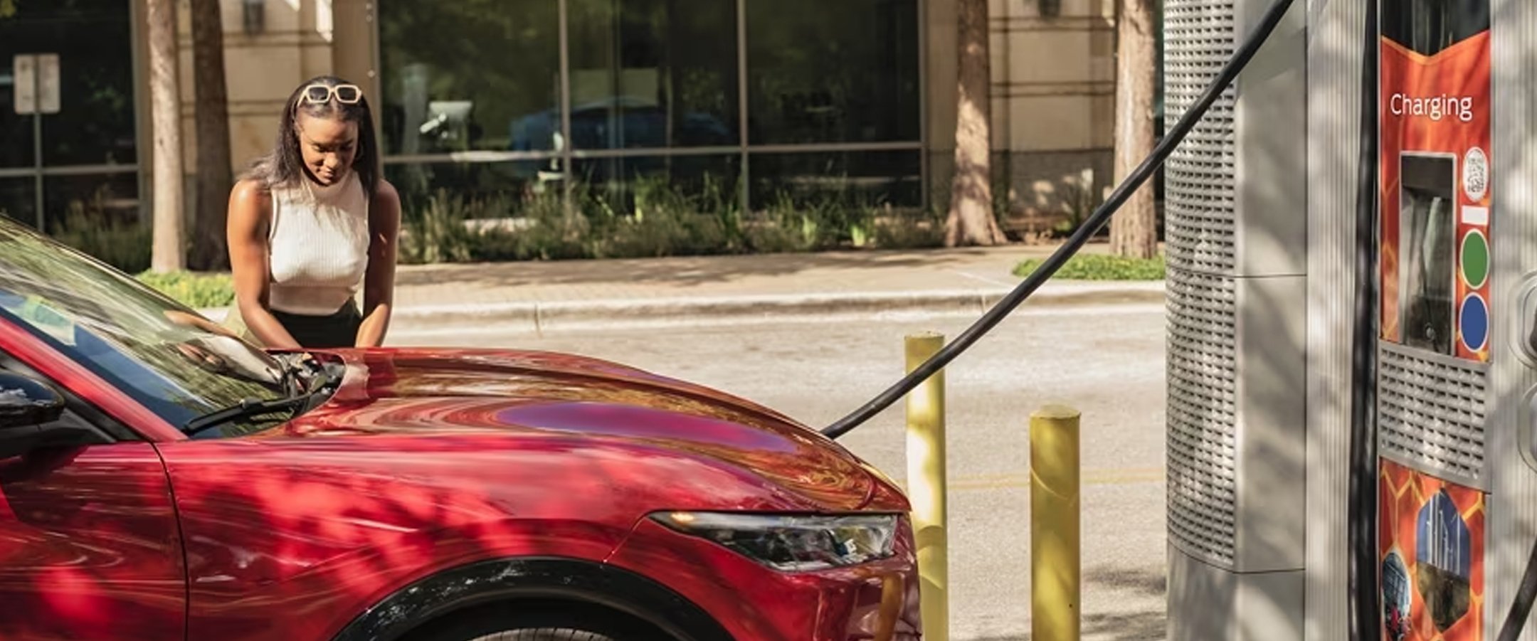 Red 2023 Mustang Mach-E being charged at a public vehicle charger.