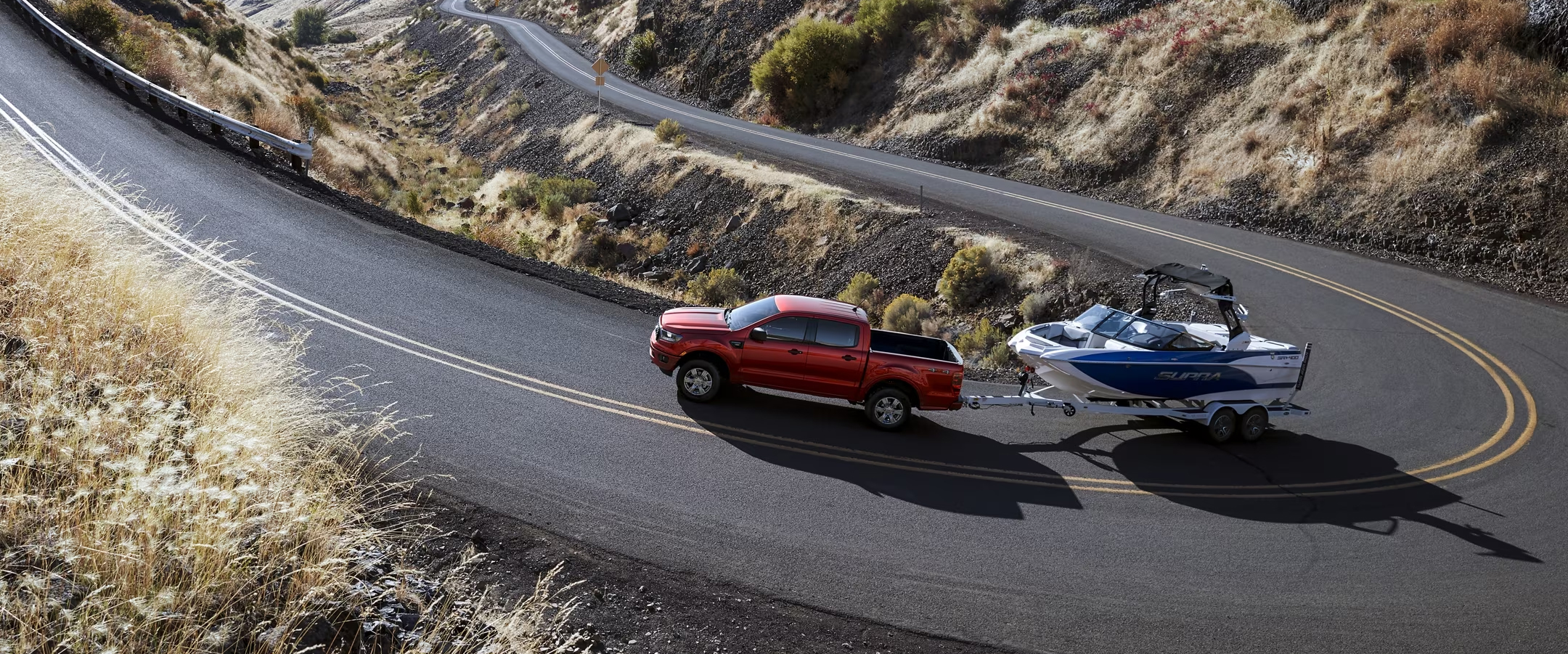 Red 2023 Ford Ranger driving up a curvy mountainside road towing a surf boat.