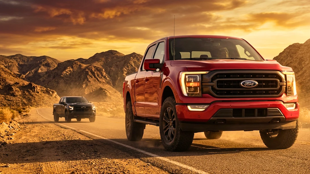 Ford F-150 rouge roulant sur une route désertique au coucher du soleil.