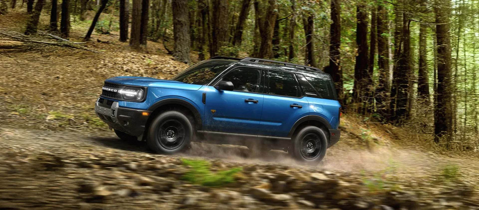 Ford Bronco Sport 2026 bleu roulant sur un sentier forestier accidenté.
