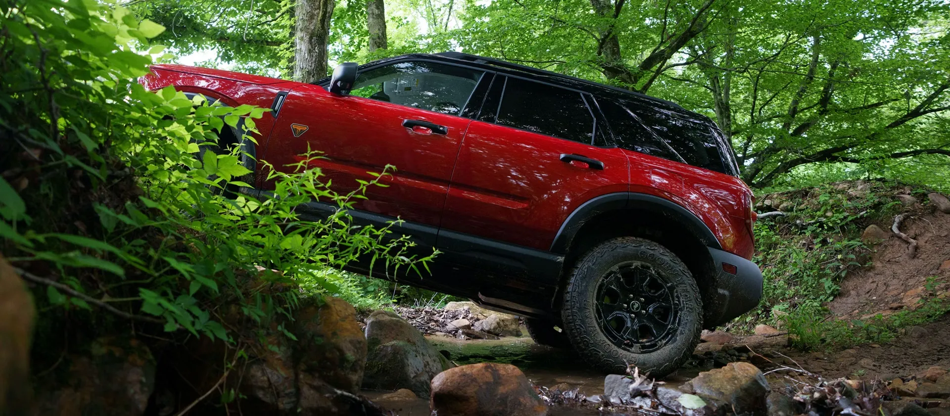 Ford Bronco Sport 2026 rouge franchissant des rochers en forêt.