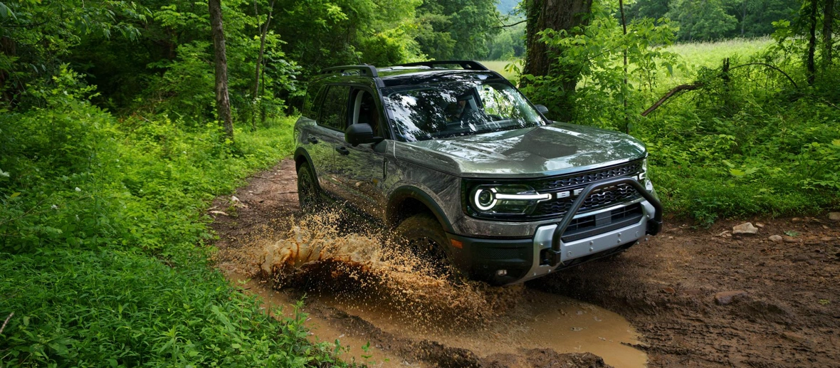 Ford Bronco Sport 2026 roulant dans la boue sur un sentier boisé.