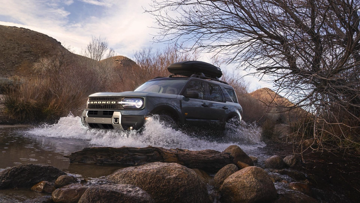 Ford Bronco Sport 2026 avec coffre de toit traversant un cours d’eau en montagne.