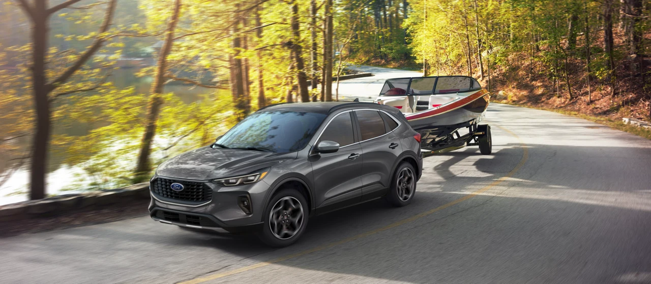 Ford Escape gris remorquant un bateau sur une route boisée.