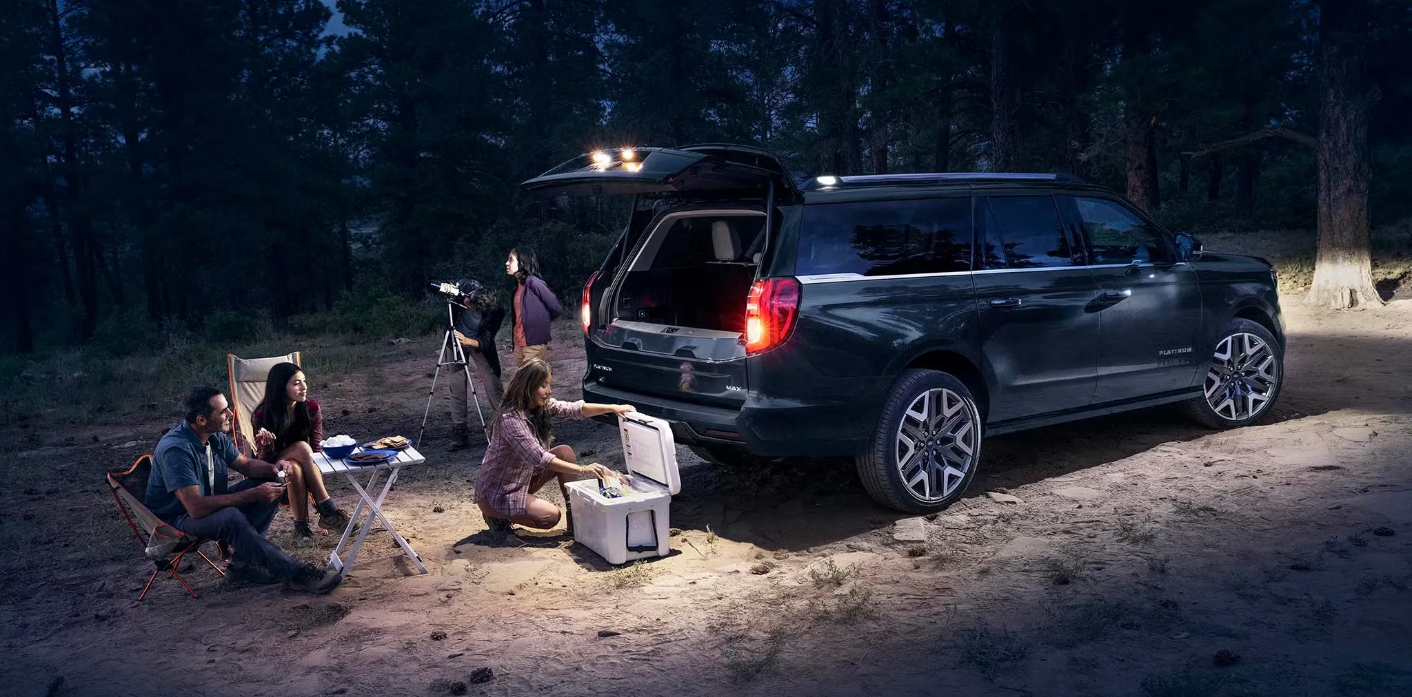 Ford Expedition 2027 avec hayon ouvert et famille installée en forêt à la tombée de la nuit.