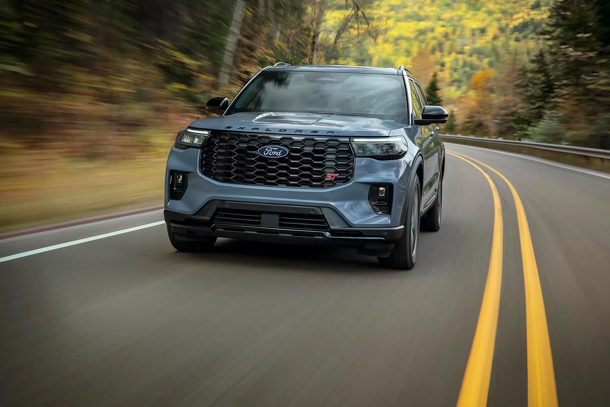 Ford Explorer 2027 roulant sur une route sinueuse bordée d’arbres aux couleurs automnales.