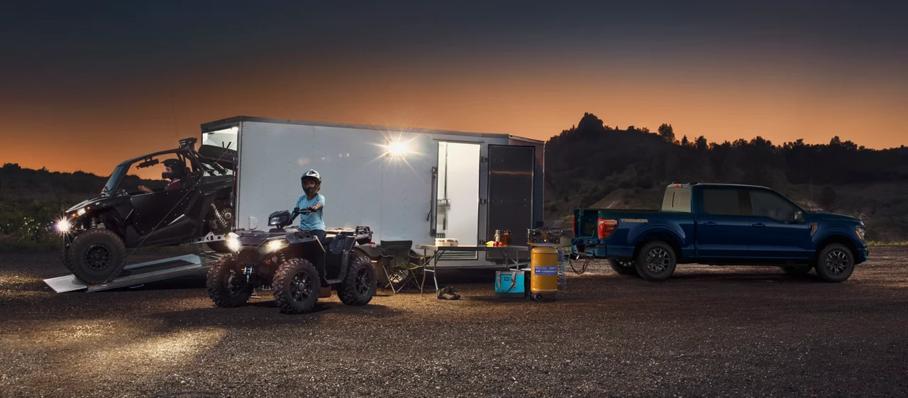 Ford F-150 bleu remorquant une roulotte avec des véhicules hors route au crépuscule.
