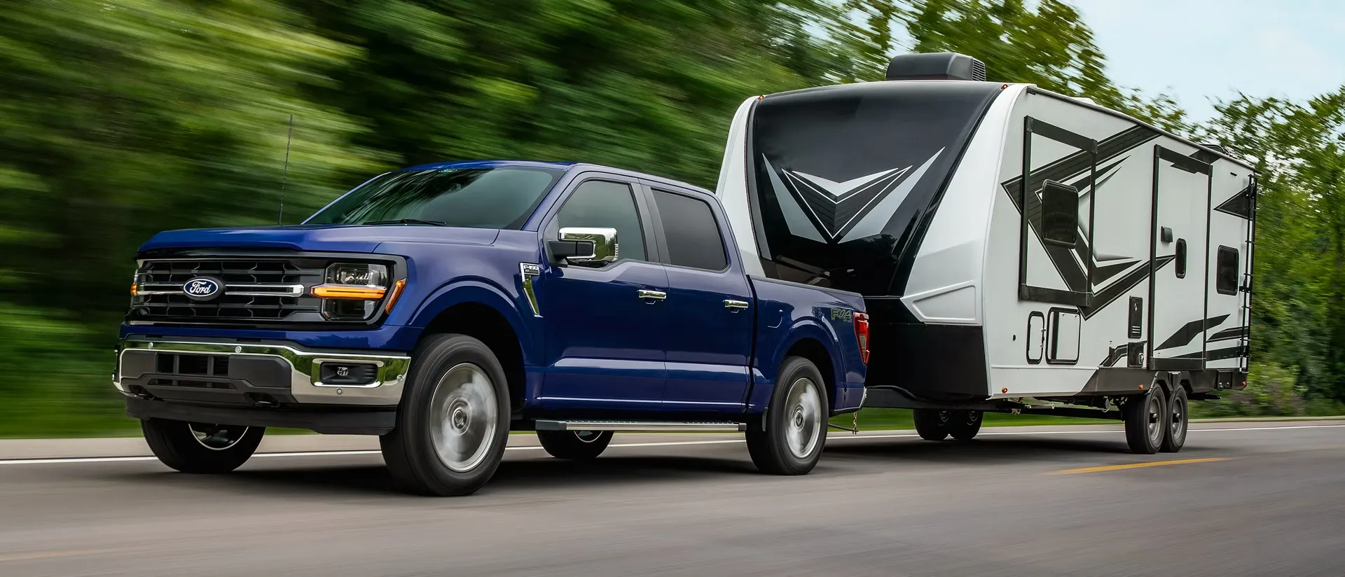 Ford F-150 2026 bleu remorquant une roulotte sur la route.
