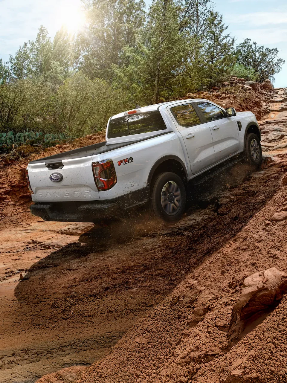 Ford Ranger 2026 blanc à cabine SuperCrew gravissant un sentier rocheux, vu de l’arrière.