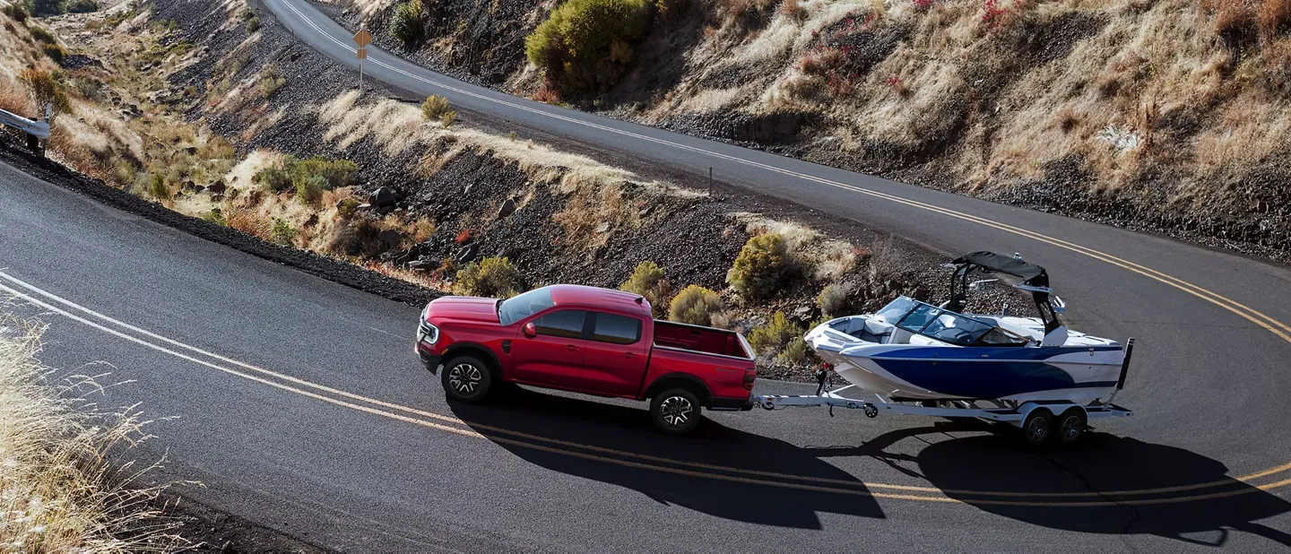 Ford Ranger 2026 rouge remorquant un bateau sur une route sinueuse en montagne.
