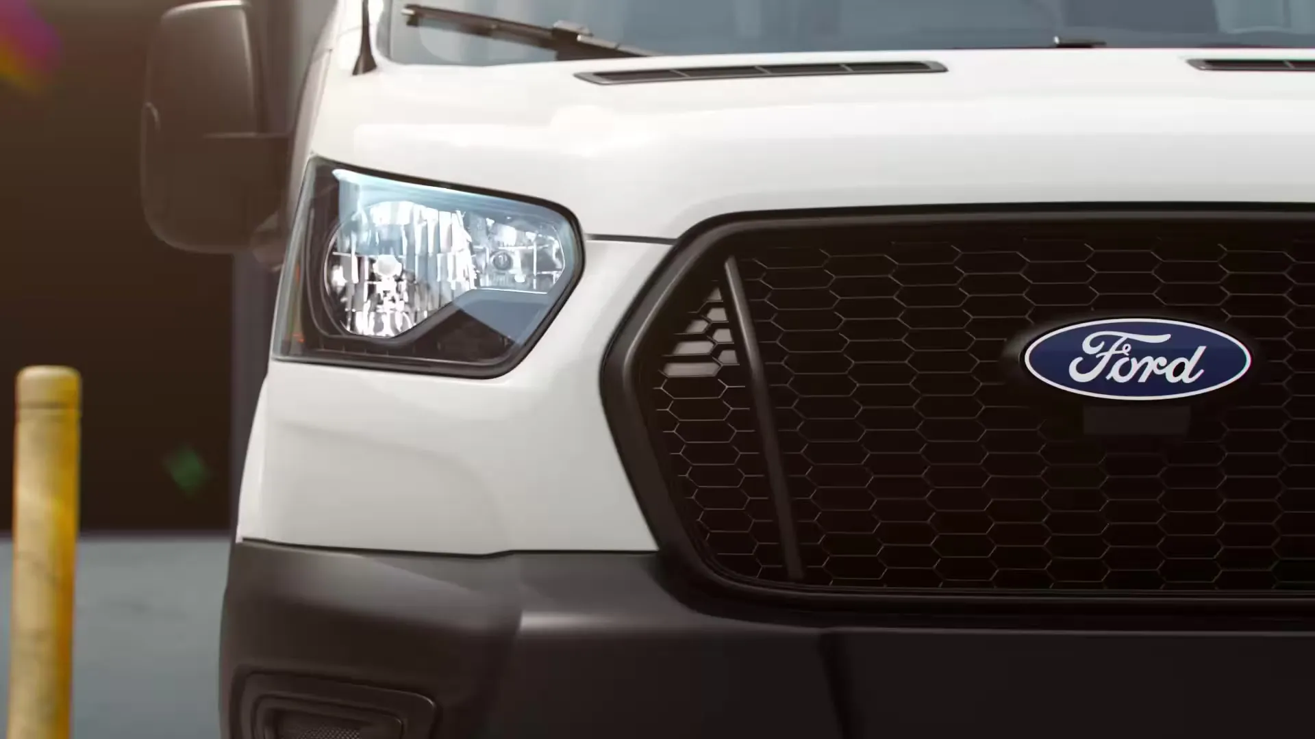 Gros plan sur le phare avant et la calandre noire avec écusson Ford d’un Transit blanc.