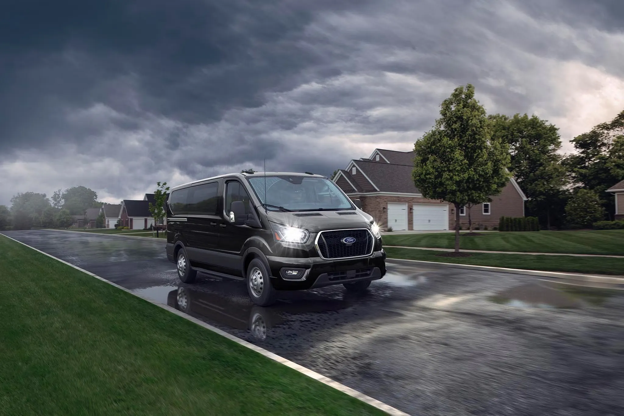 Ford Transit gris roulant sur une chaussée mouillée dans un quartier résidentiel.