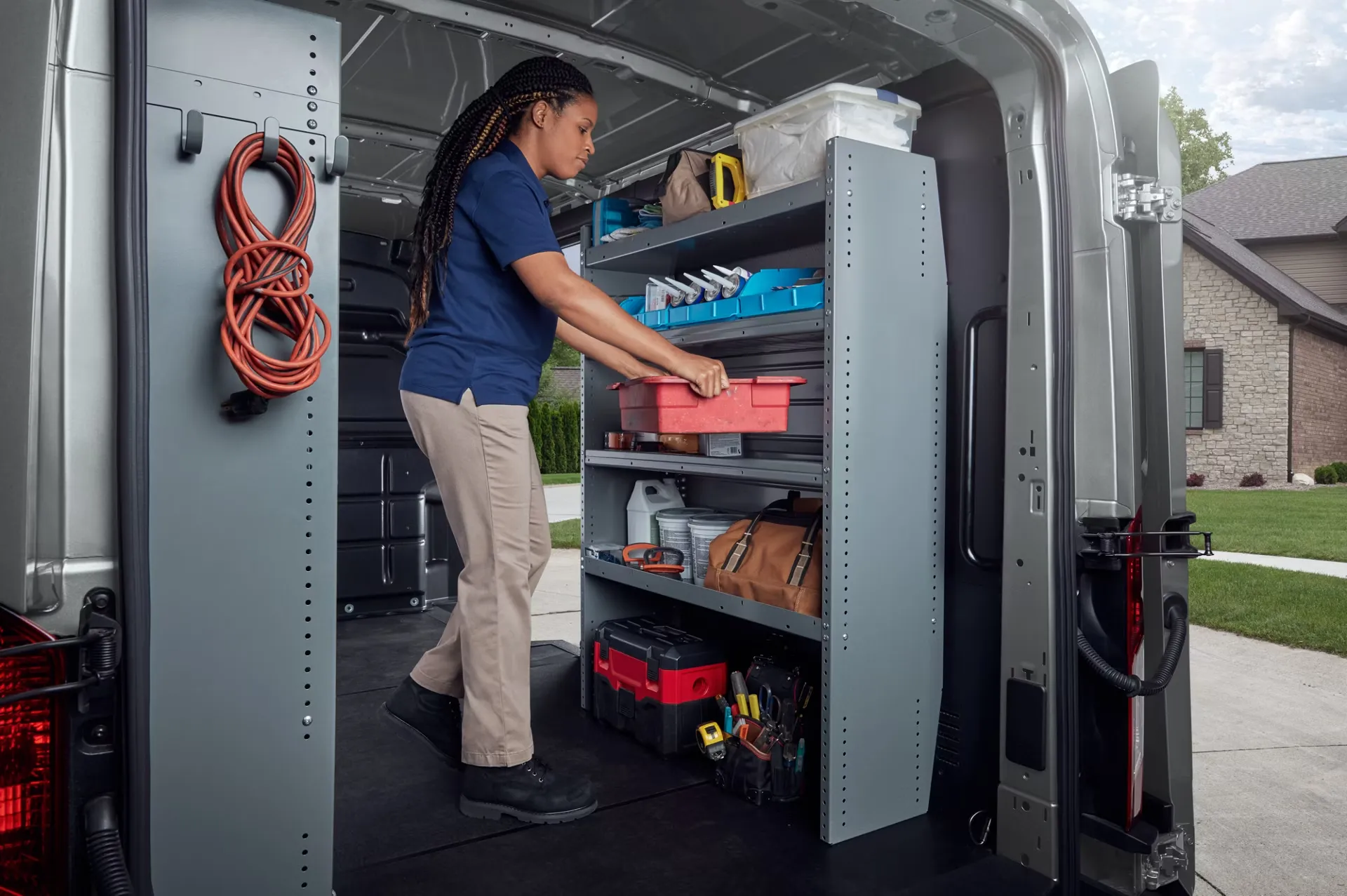 Espace de chargement d’un Ford Transit aménagé avec des étagères, où une travailleuse range ses outils.