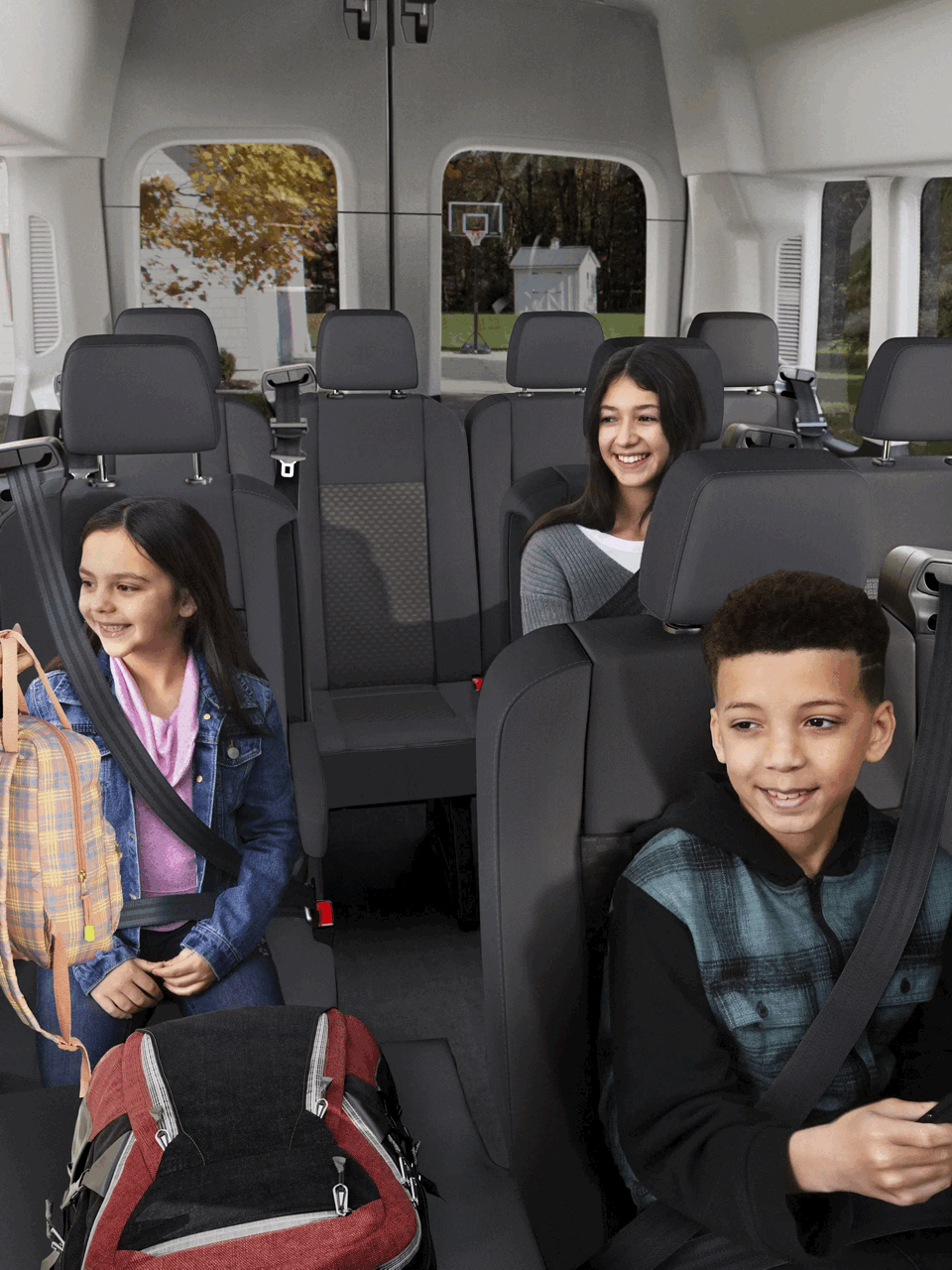 Intérieur d’un Ford Transit pour passagers avec plusieurs rangées de sièges et des enfants attachés.