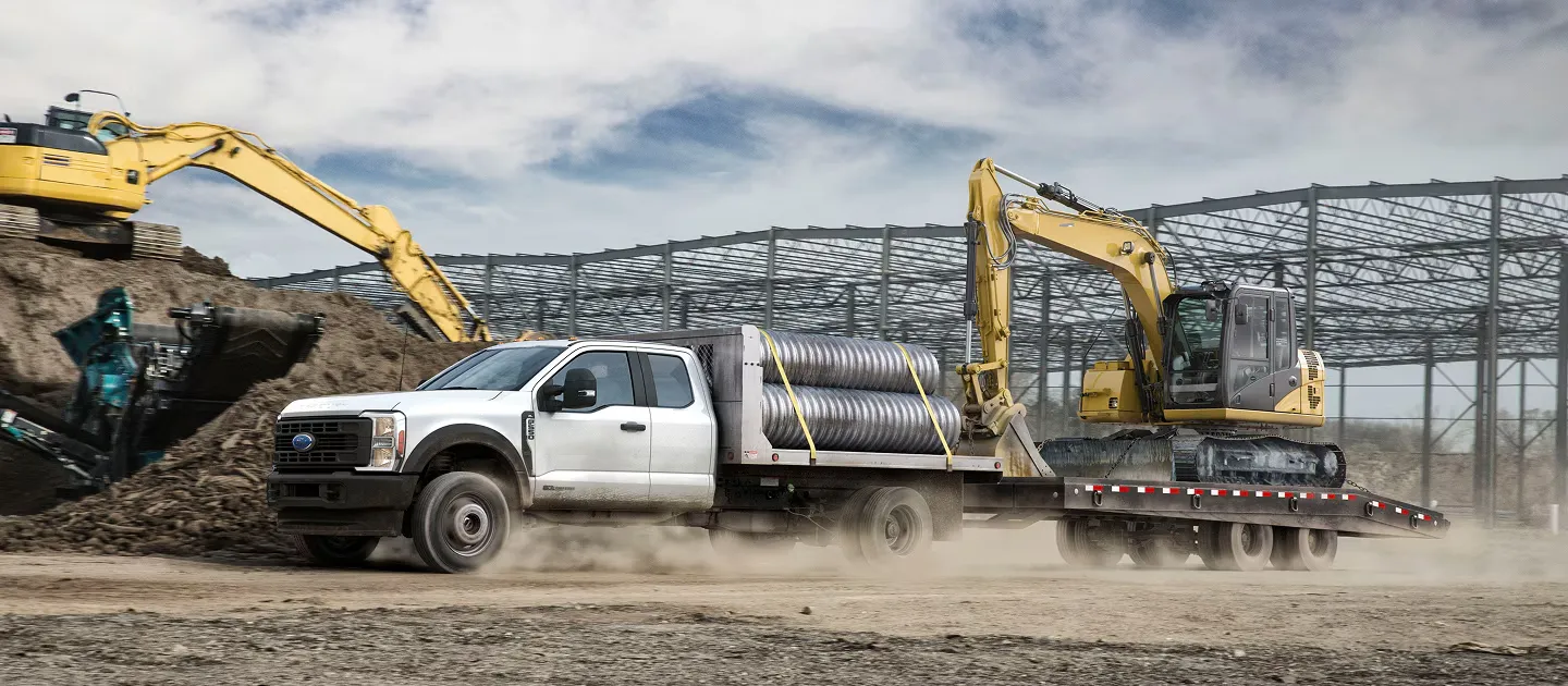 Ford F-550 Super Duty Châssis-cabine remorquant une excavatrice sur un chantier.