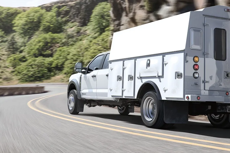 Camion de service Ford Châssis-cabine blanc circulant sur une route sinueuse.