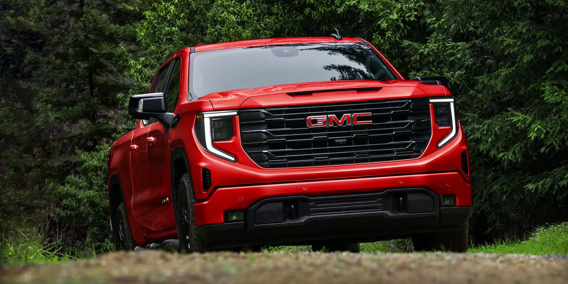 GMC Sierra 1500 2026 rouge présenté devant un paysage boisé.