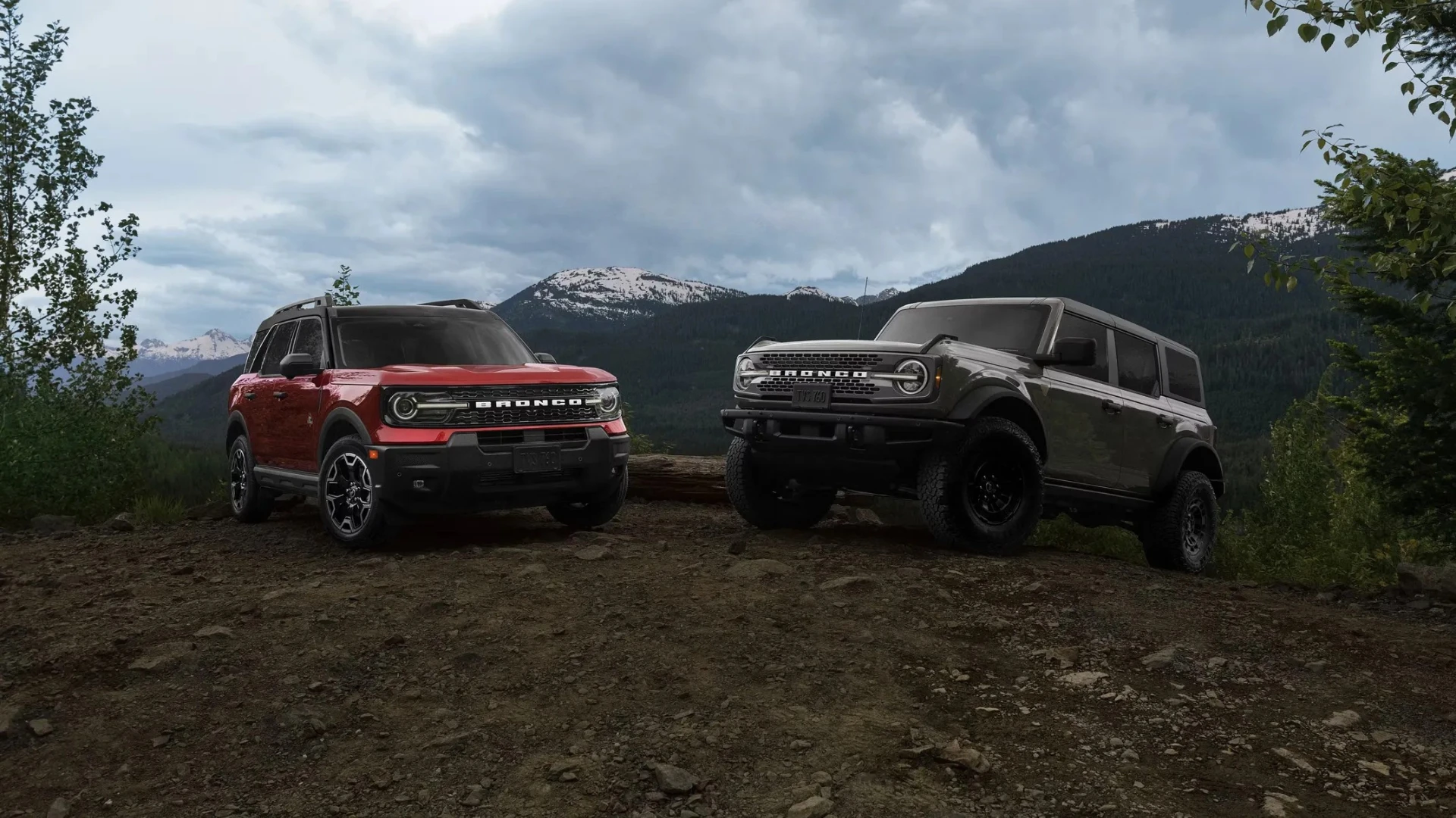 Ford Bronco Sport 2026 rouge et Ford Bronco 2026 gris sur un sentier montagneux.