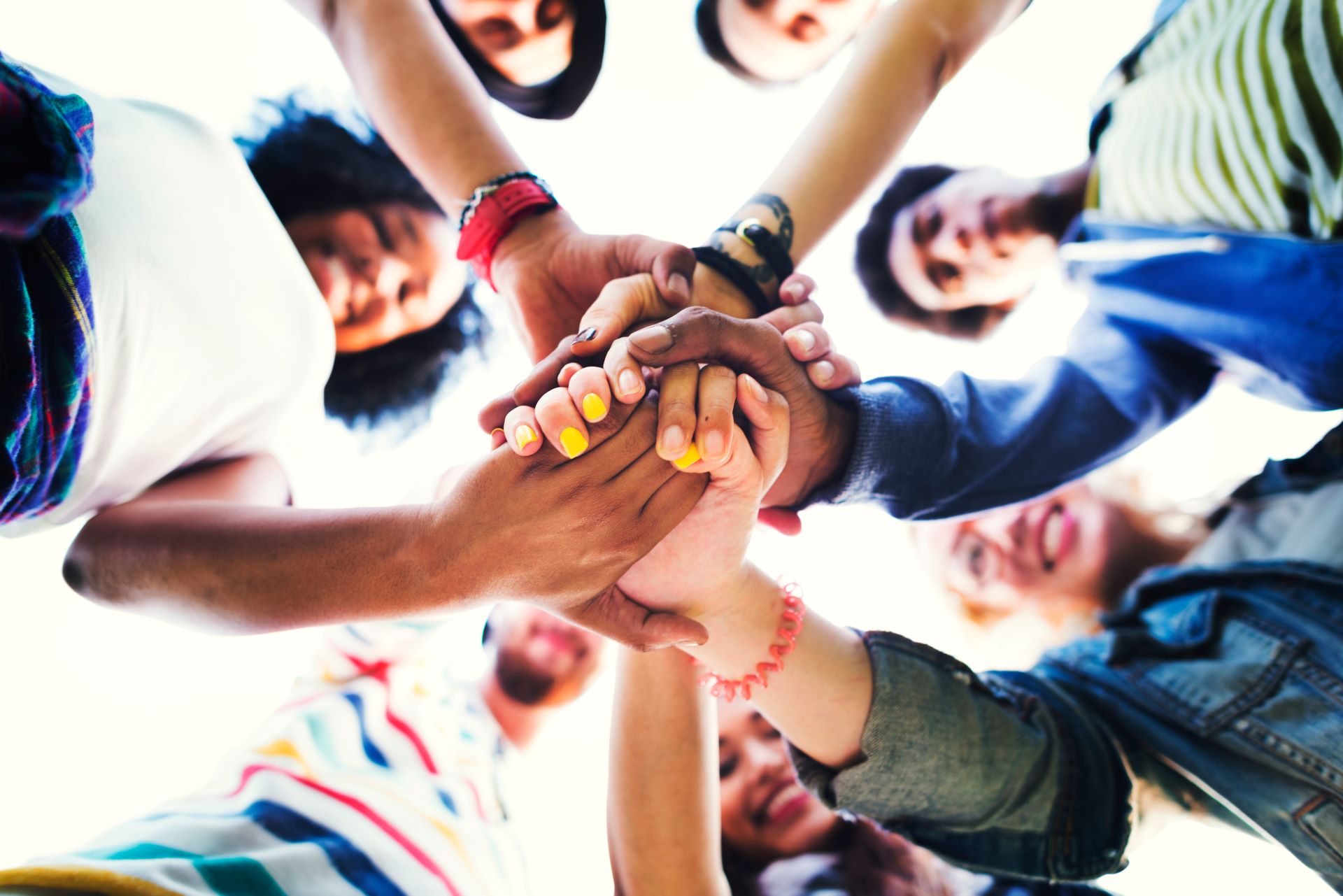 concept of community with diverse group shot low angle with clasped hands looking down at camera