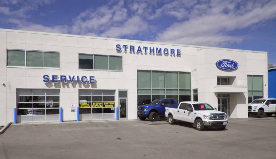 Exterior shot of Strathmore Ford at high noon on a summer day with two Ford trucks parked in front of the entrance